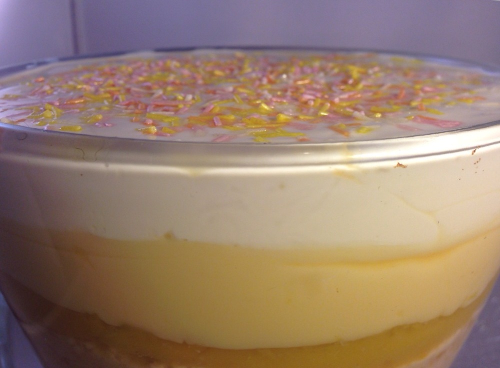 custard and cream layers on top of orange and mango trifle complete with sugar sprinkles